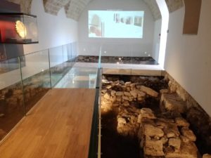 Particolare della illuminazione dei resti archeologici sotto la passerella e visione anche della videoproiezione sullo sfondo nella sala 6