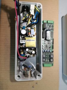 Scheda Digiled a lato (pixelata per riservatezza della tecnologia proprietaria) ed alimentatore dentro la scatola. Una scheda Digiled è composta da un sistema a microcotrollore programmabile che permette di alimentare e regolare 4 lampade o faretti led